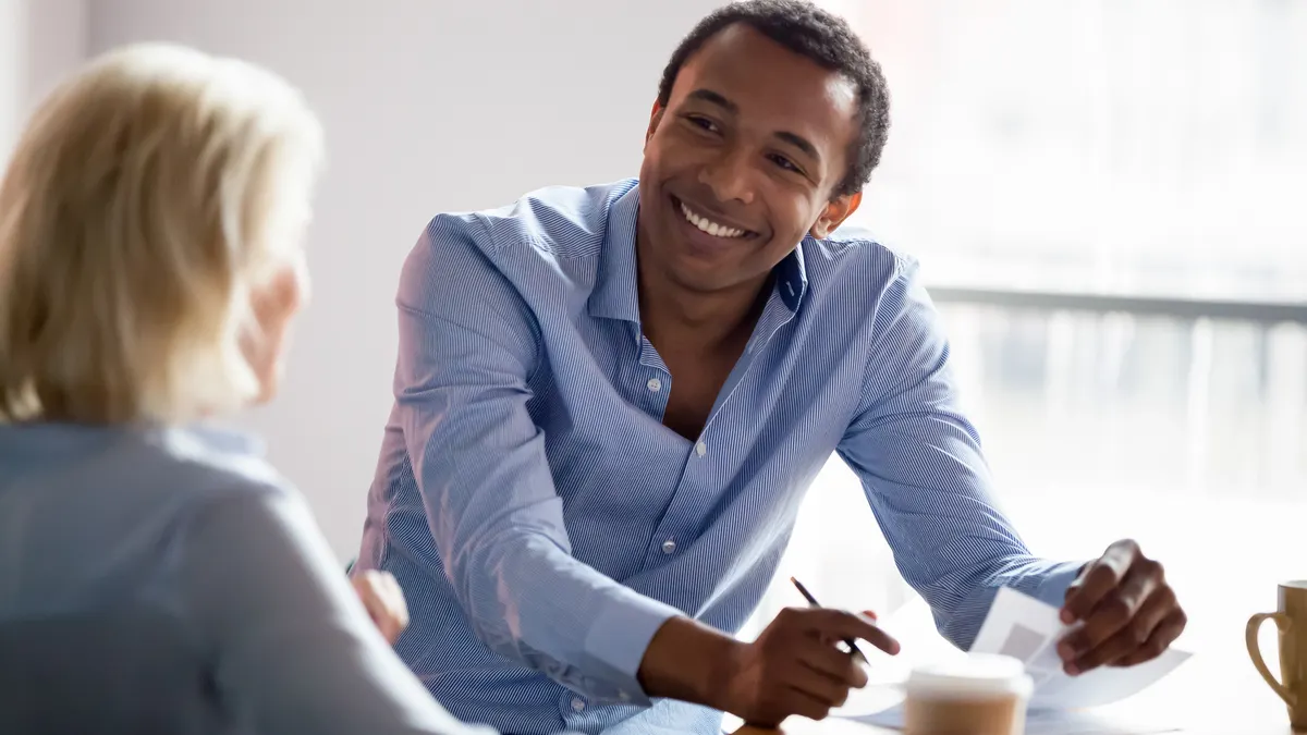 Young male in the office smiling happily at his colleague with a pen and paper in hand