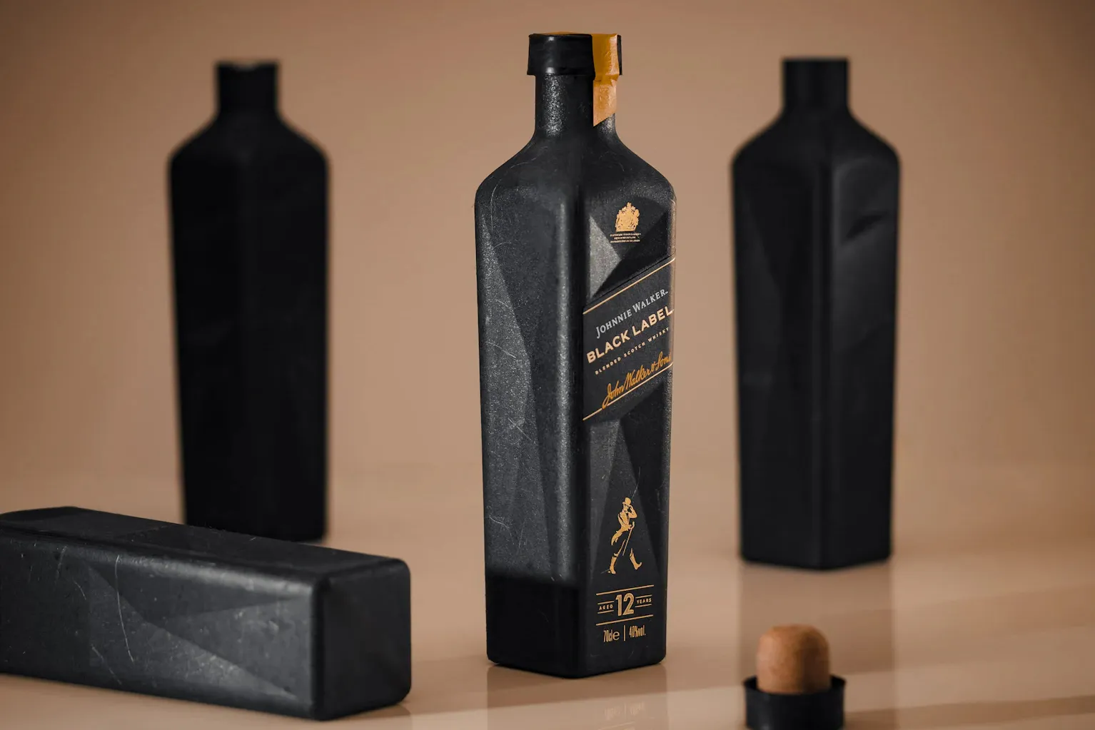 A black bottle labeled, “Johnnie Walker Black Label Blended Scotch Whiskey” stands in middle of duplicate bottles on a tan background.