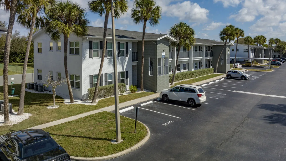 Two-level apartment property surrounded by palm trees, cars and a parking lot