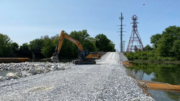 A backhoe sits on a causeway near electric power lines.