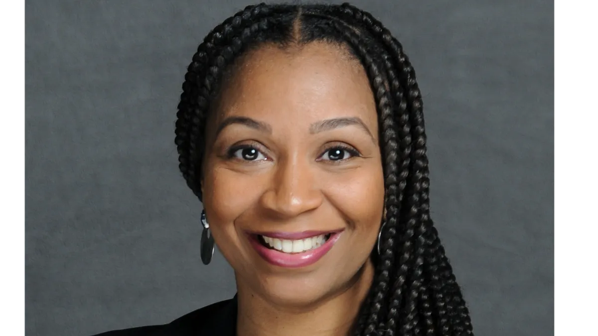 An image of a woman in a suite in front of a gray background.