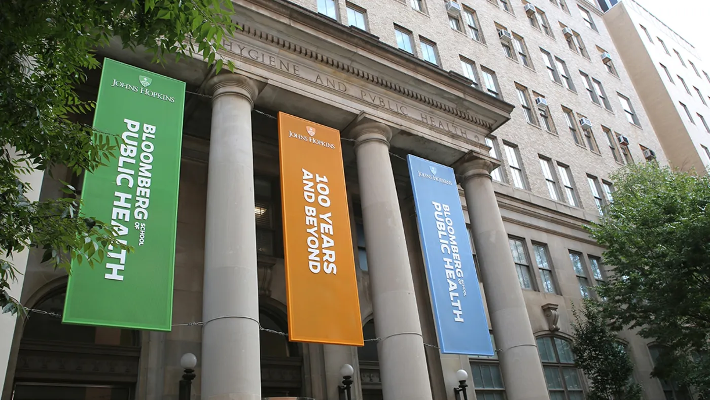 The front of an academic building with coliseum pillars. Between the pillars are hanging banners in orange, green and blue.