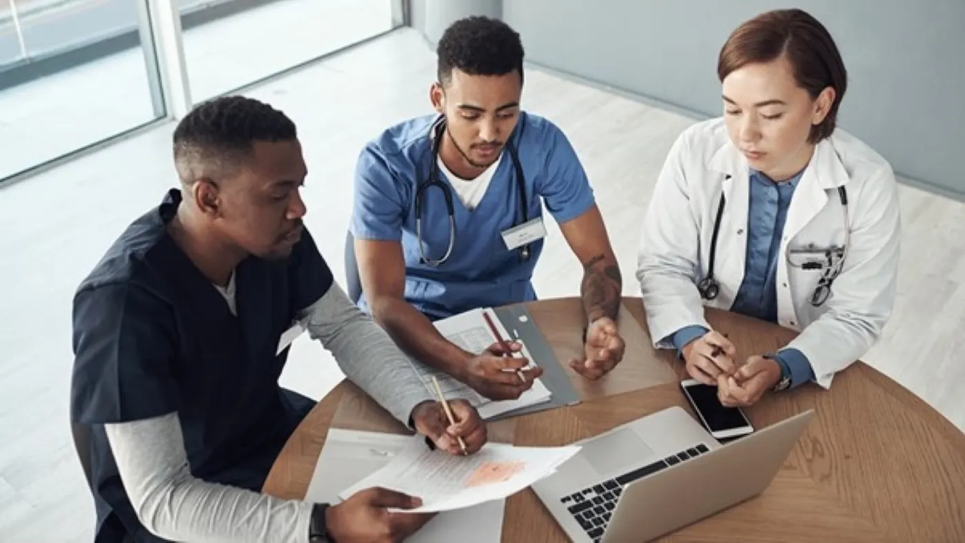 Small group of medical professionals having a meeting while reviewing reports and a laptop