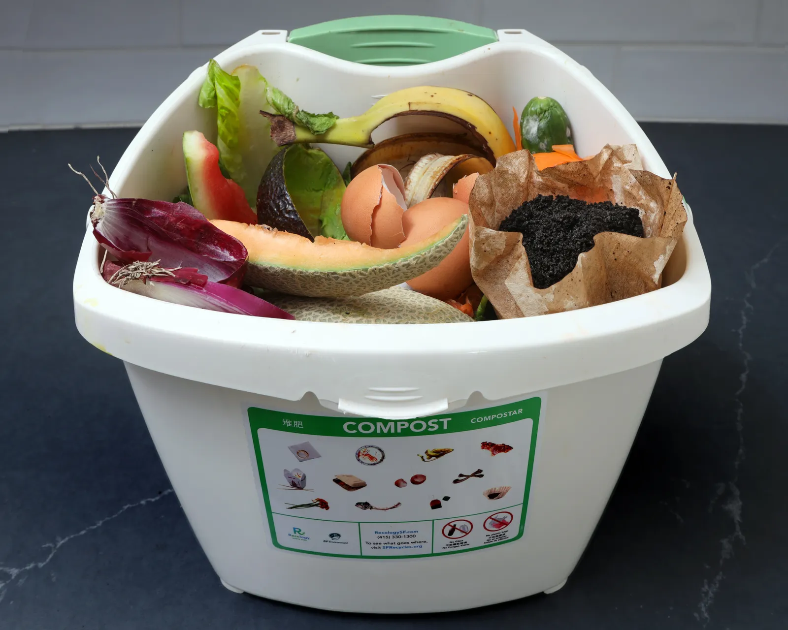 A small white plastic pail with food scraps and a label on composting guidelines