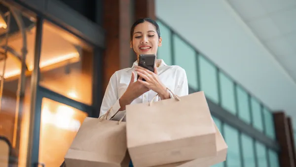 Woman online shopping through cellphone while at the mall, holding shopping bags