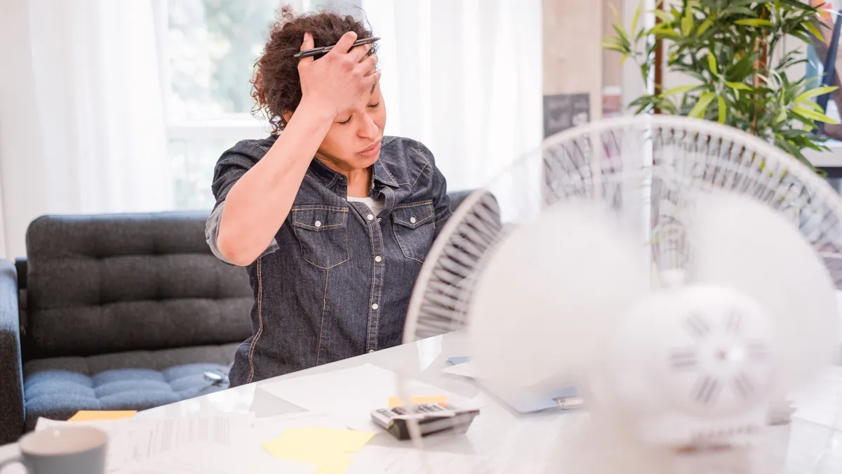 A woman wipes sweat from her brow while working at a desk.