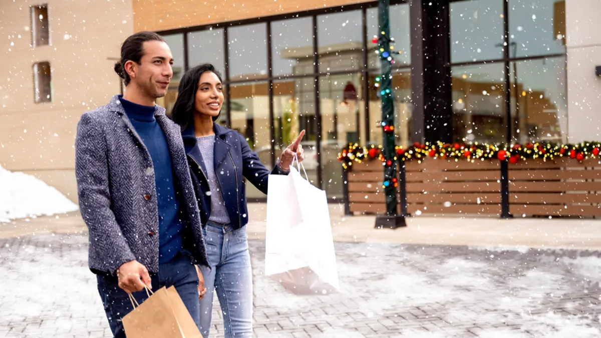 Two people walking down snowy sidewalk holding shopping bags