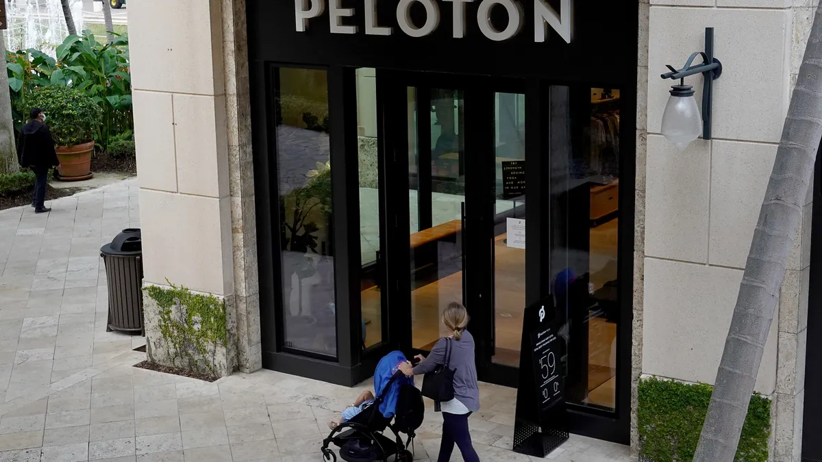 A person walks by a Peloton store while wheeling a stroller.