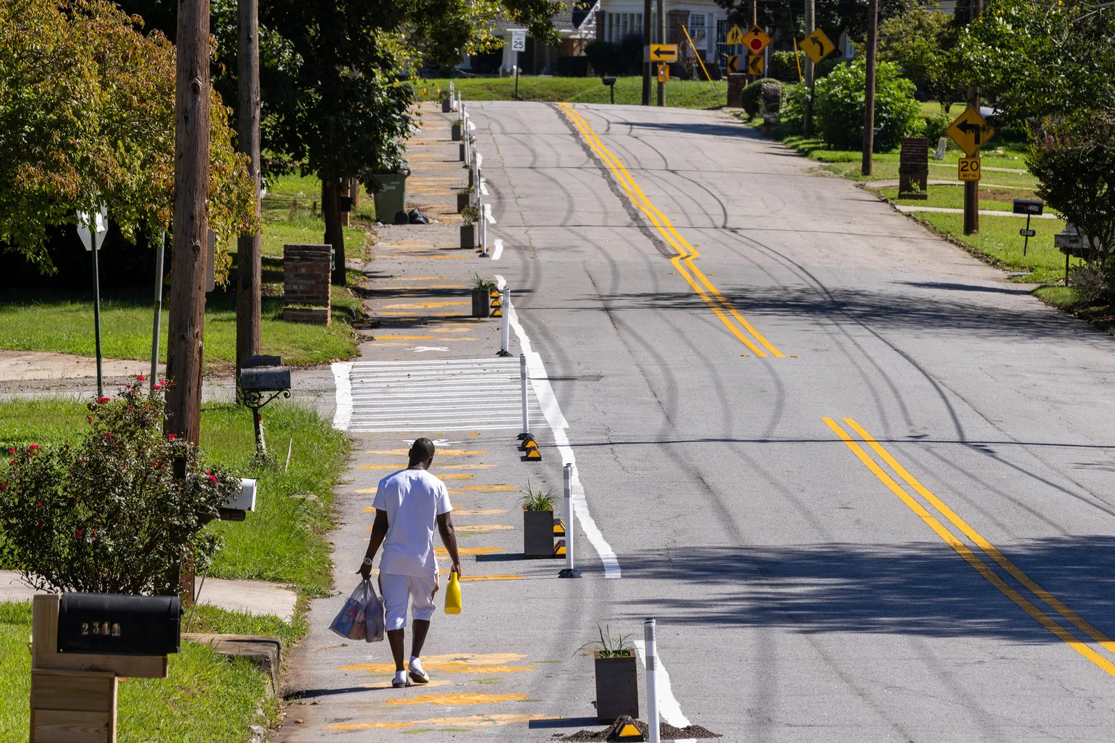 A lone man walks alongside a roadway carrying grocery bags.