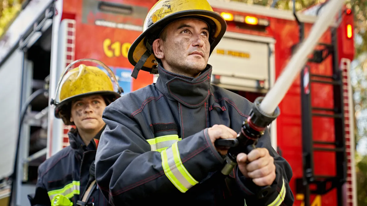 Low angle view of Caucasian first responders in their 30s holding and supporting nozzle as it shoots straight stream of water.