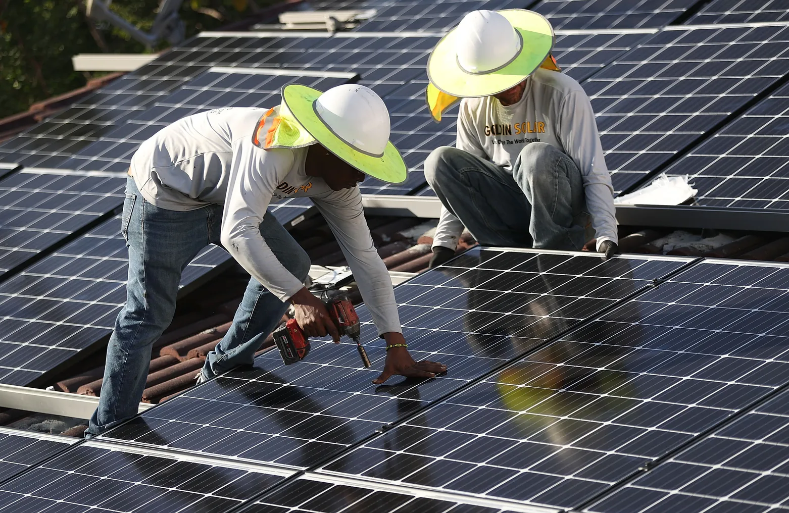 Workers install solar panels on the roof of a building.