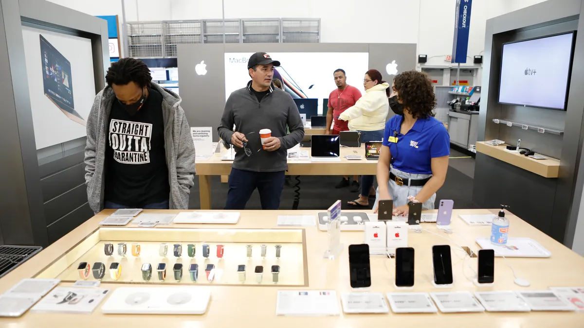 A worker assists a man in front of a display of Apple products.