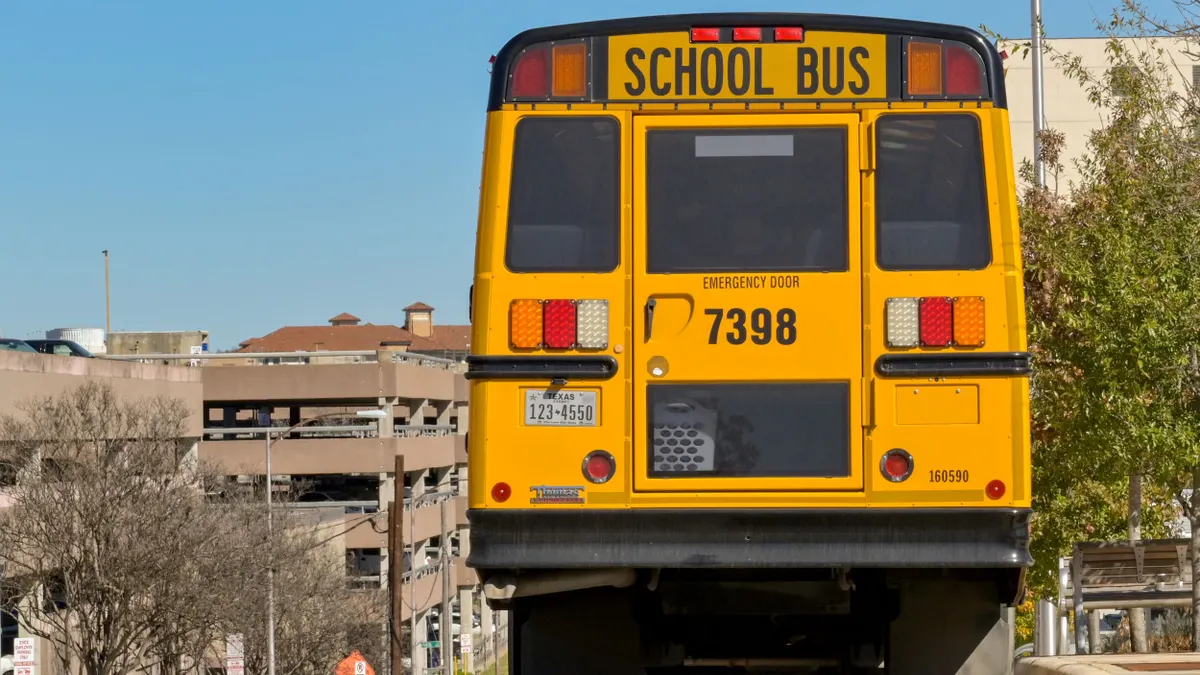 A rear view of a yellow school bus at the top of a hill with a Texas license plate.