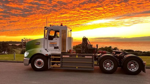 A battery-electric semi-truck with a sunset and water in the background.