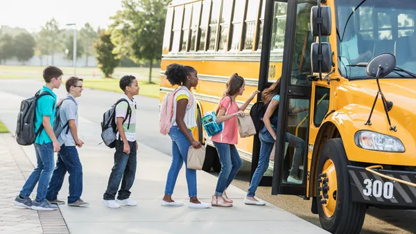 Students line up and board a yellow school bus on a sunny day. Each child carries a backpack, conveying a sense of routine and anticipation.