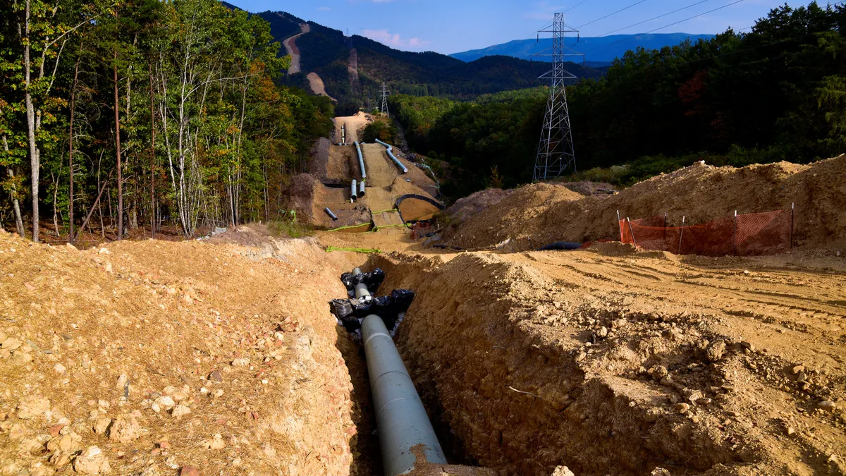 A large white pipe lies in a dirt trench, stretching toward mountains in the background.