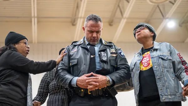 A person wearing a police uniform prays as two other people touch them.