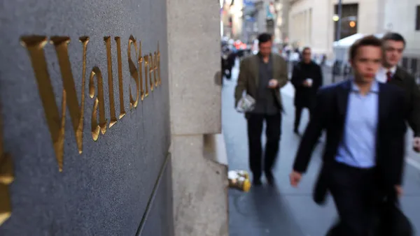 Image of business people walking past building with Wall Street sign.