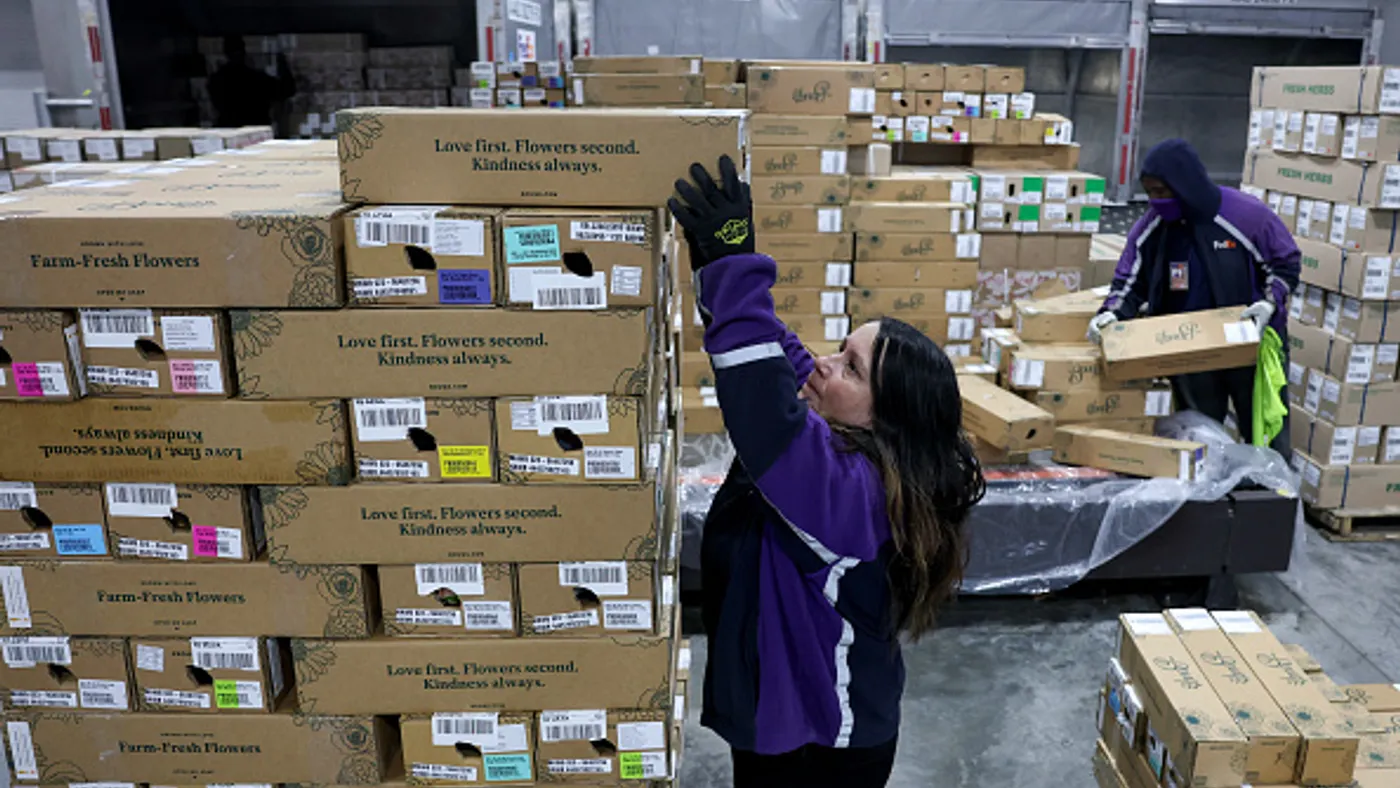 Employees stack packages containing flowers in a warehouse.