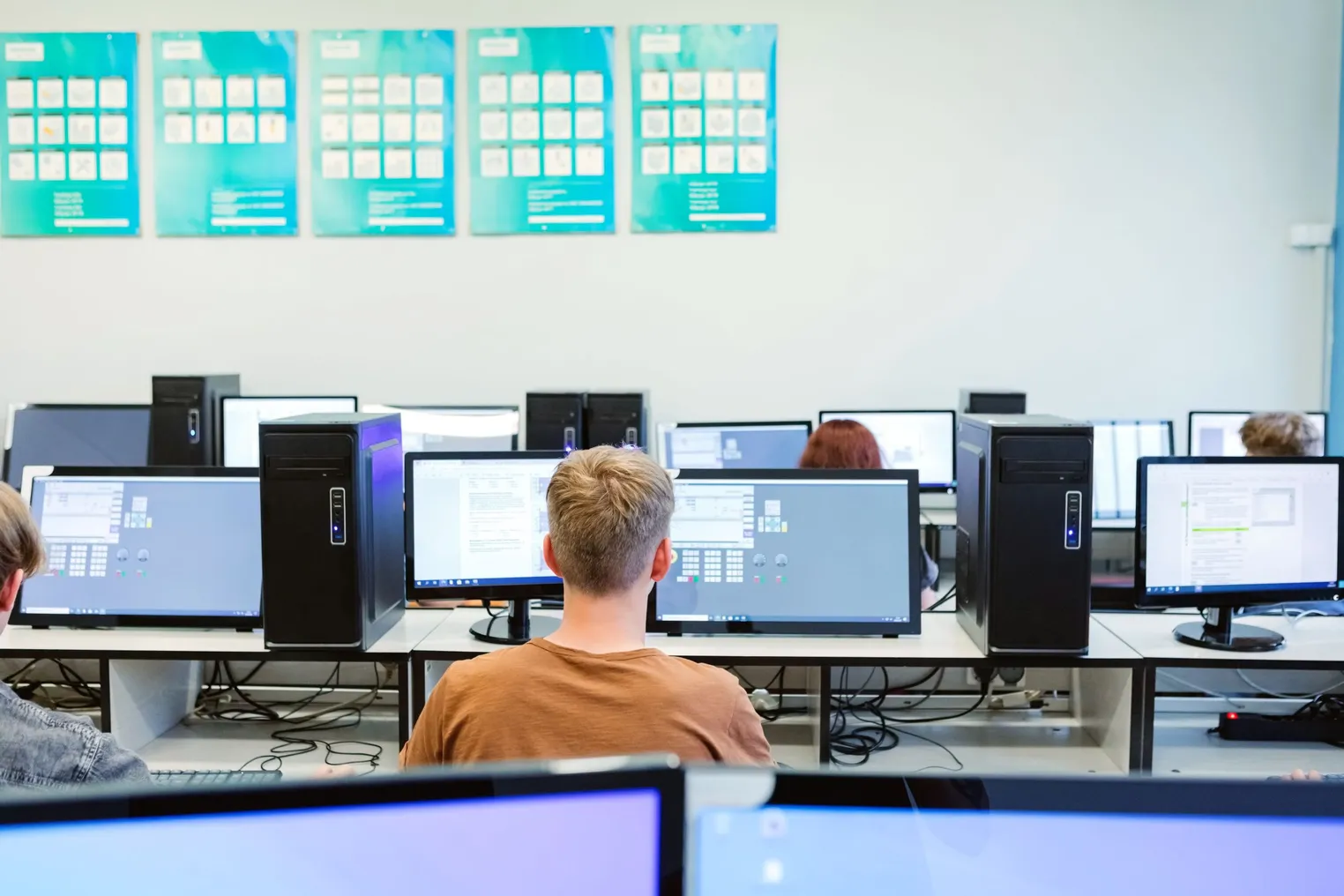 A row of students learning how to code while working at a classroom computer.