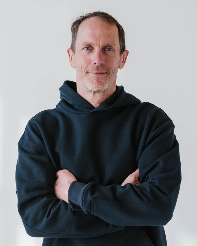 A headshot of a man in a hoodie crossing his arms.