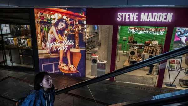 In a mall, a person rides an escalator in front of a Steve madden store.