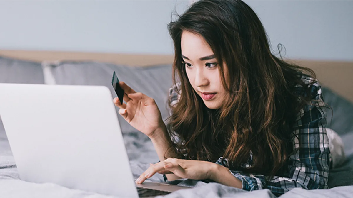 A woman looking at her laptop holding a payment card.