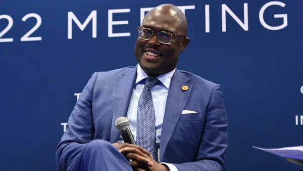 A man wearing a suit sits on a chair with a microphone.