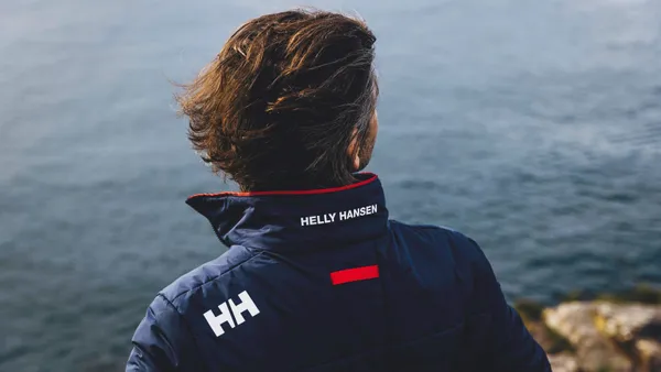 A person wearing a Helly Hansen-branded wind breaker over looks a sea.