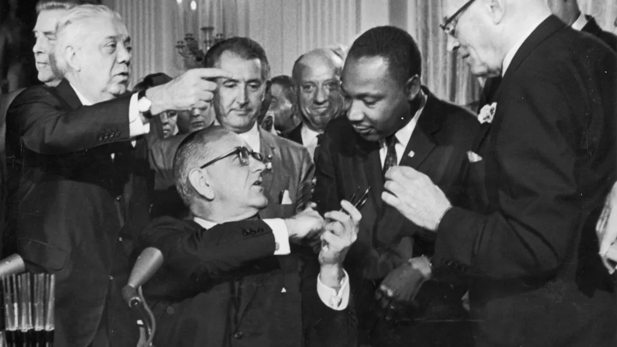 President Lyndon B. Johnson shakes the hand of Martin Luther King Jr. at the signing of the Civil Rights Act in Washington, D.C., as officials look on.