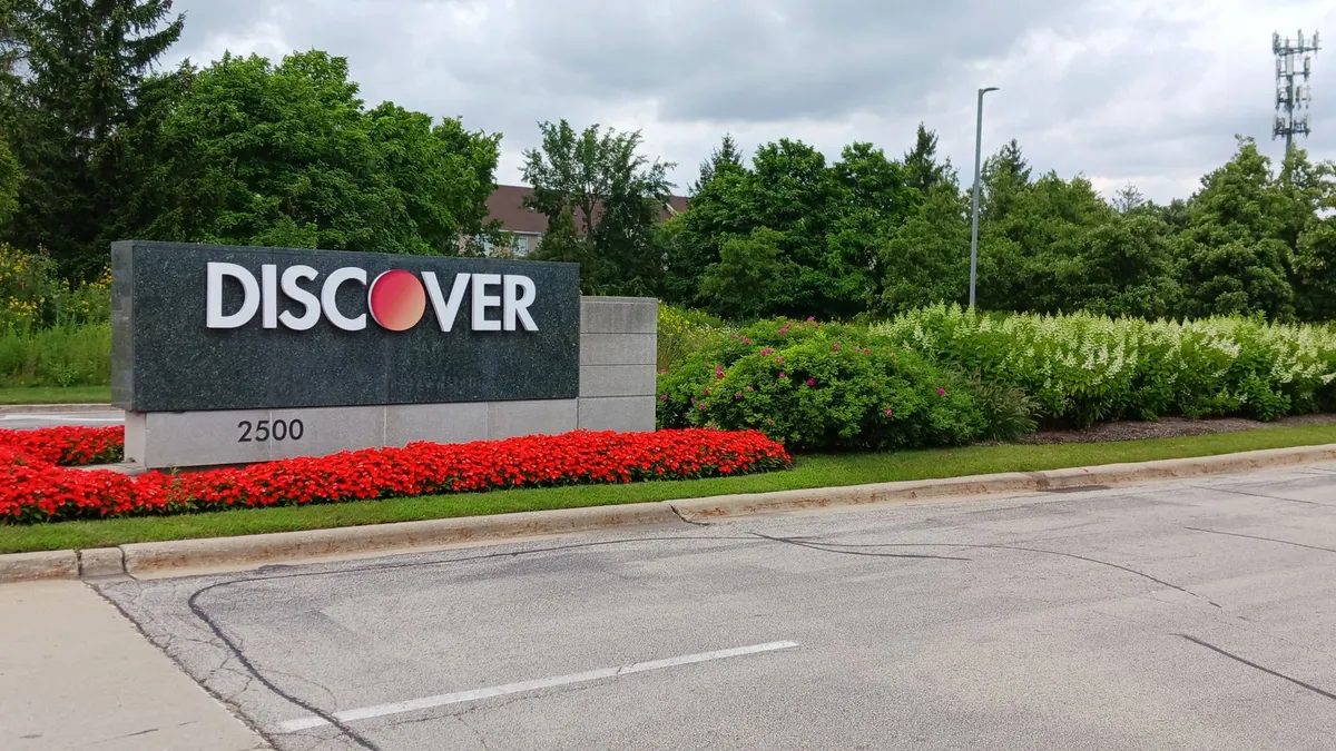 Discover sign at driveway entrance to headquarters with flowers in front.