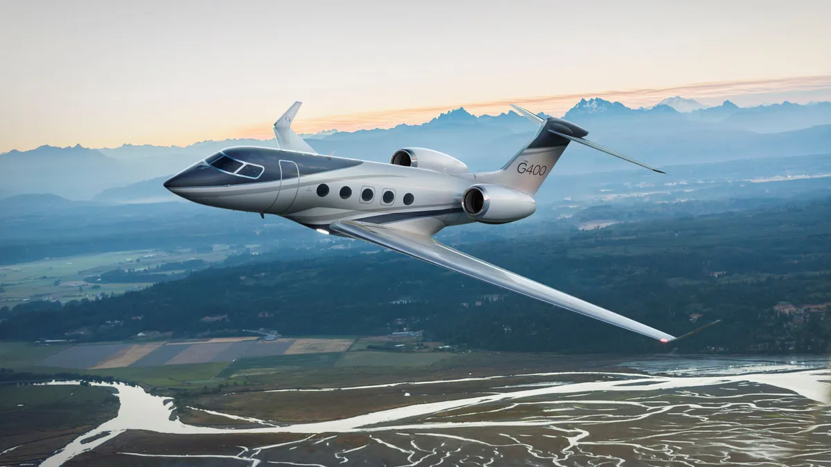 A Gulfstream aircraft flies in the sky over a body of water. with mountains in the background.