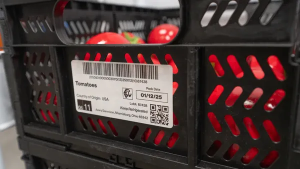 A black plastic crate filled with tomatoes has a label on the exterior indicating the contents.