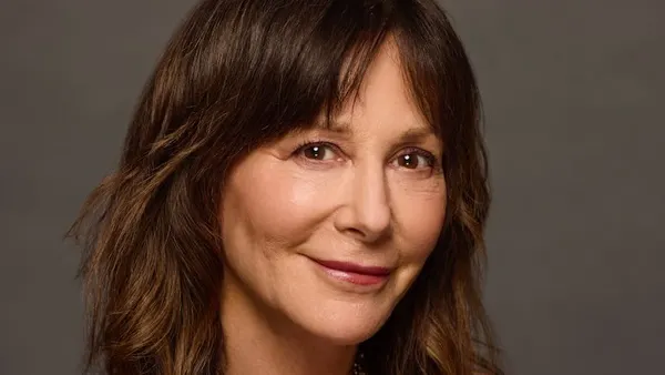 A person with long brown hair smiles.