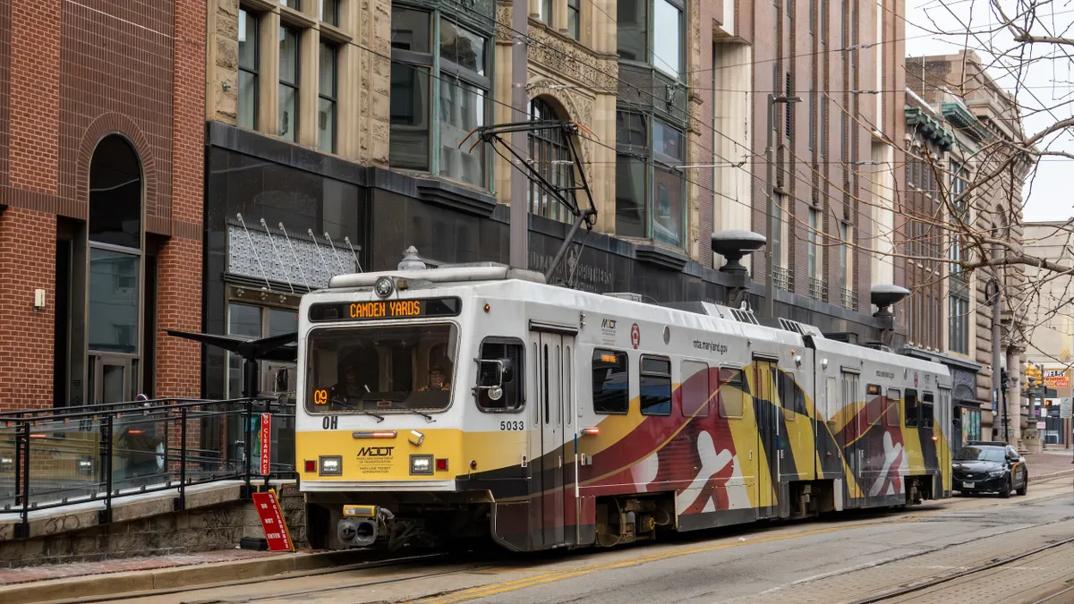 A 2-car tram under an electric wire on a street with buildings behind it.