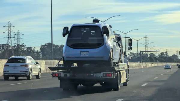 A blue vehicle on a flatbed truck along a highway with other cars.
