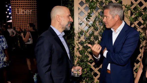 Two people in suits speaking to each others with more people in the background.