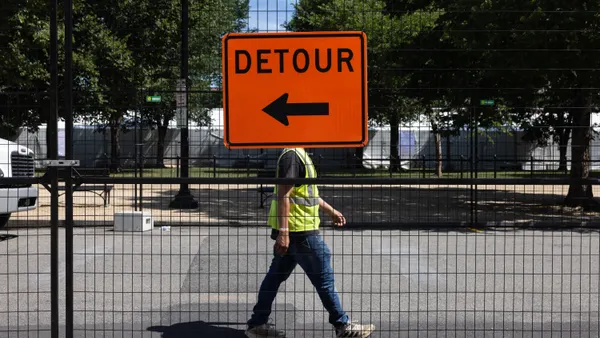 A construction worker walks on the street next to a detour sign.