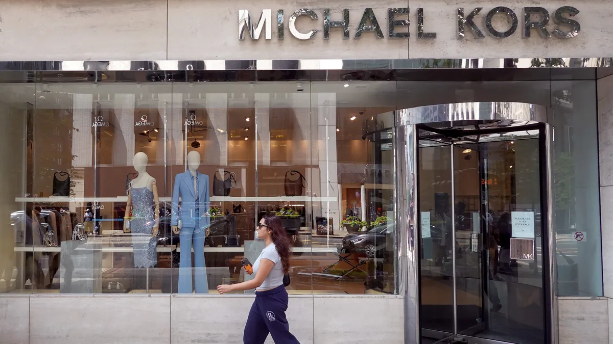 A pedestrian in short sleeves walks past a Michael Kors storefront on a sunny day in Chicago, Illinois.