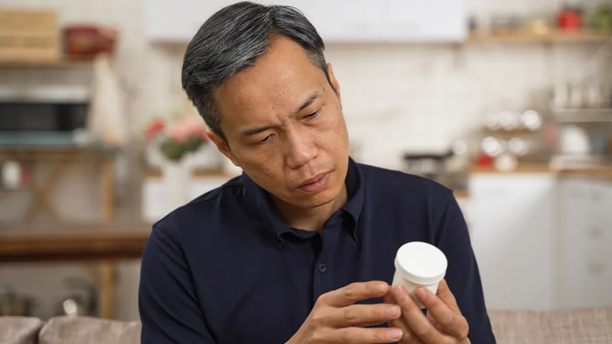 Man in living room looking at pill bottle.