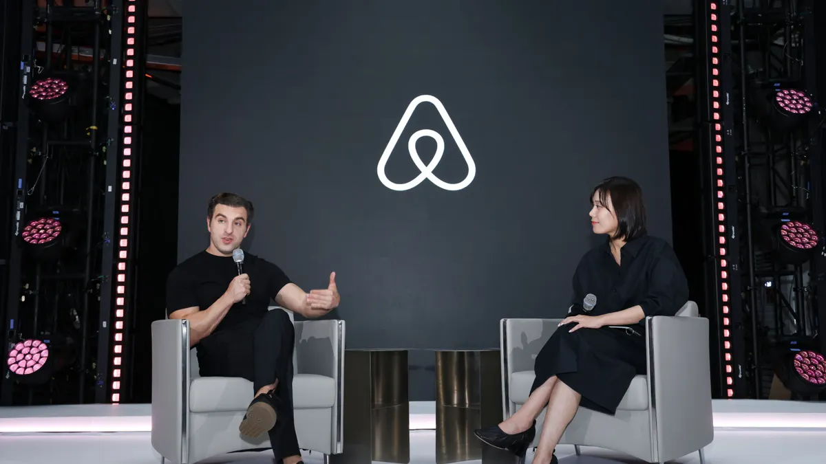 Two people sit on a stage with an Airbnb logo as the backdrop.