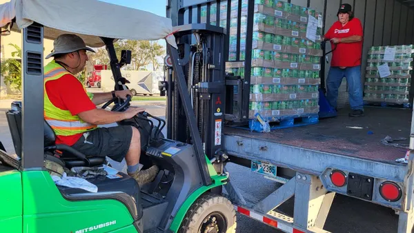 A forklift driver loads a truck with canned goods.