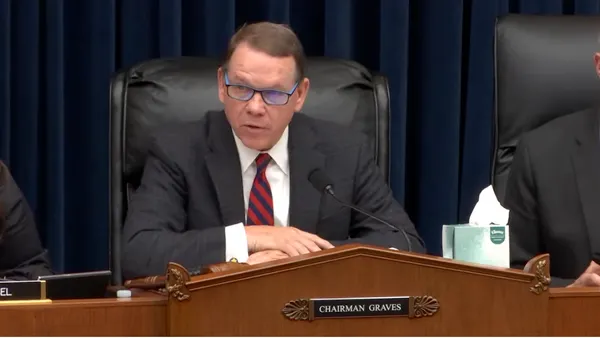 A seated man in a dark suit at desk with a nameplate reading "Chairman Graves."