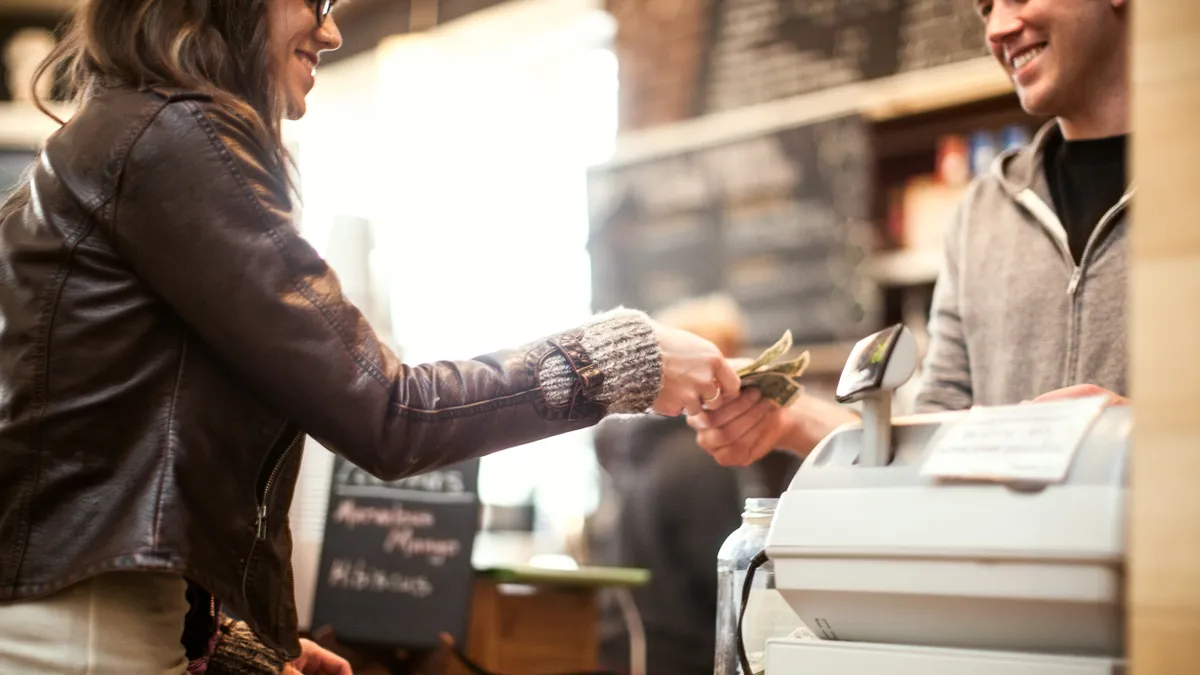 Woman hands cash to cashier at small shop.