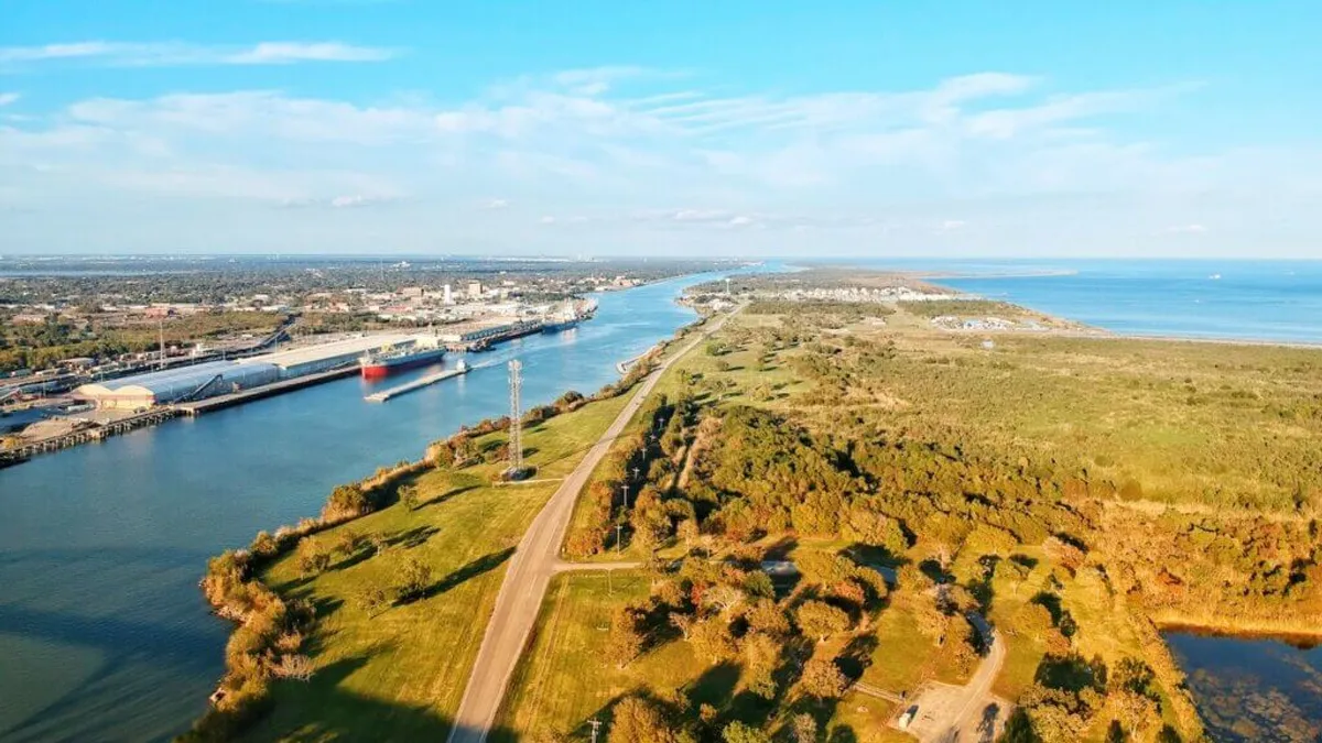 Aerial view of a channel with a red ship in it leading out to a bigger body of water.