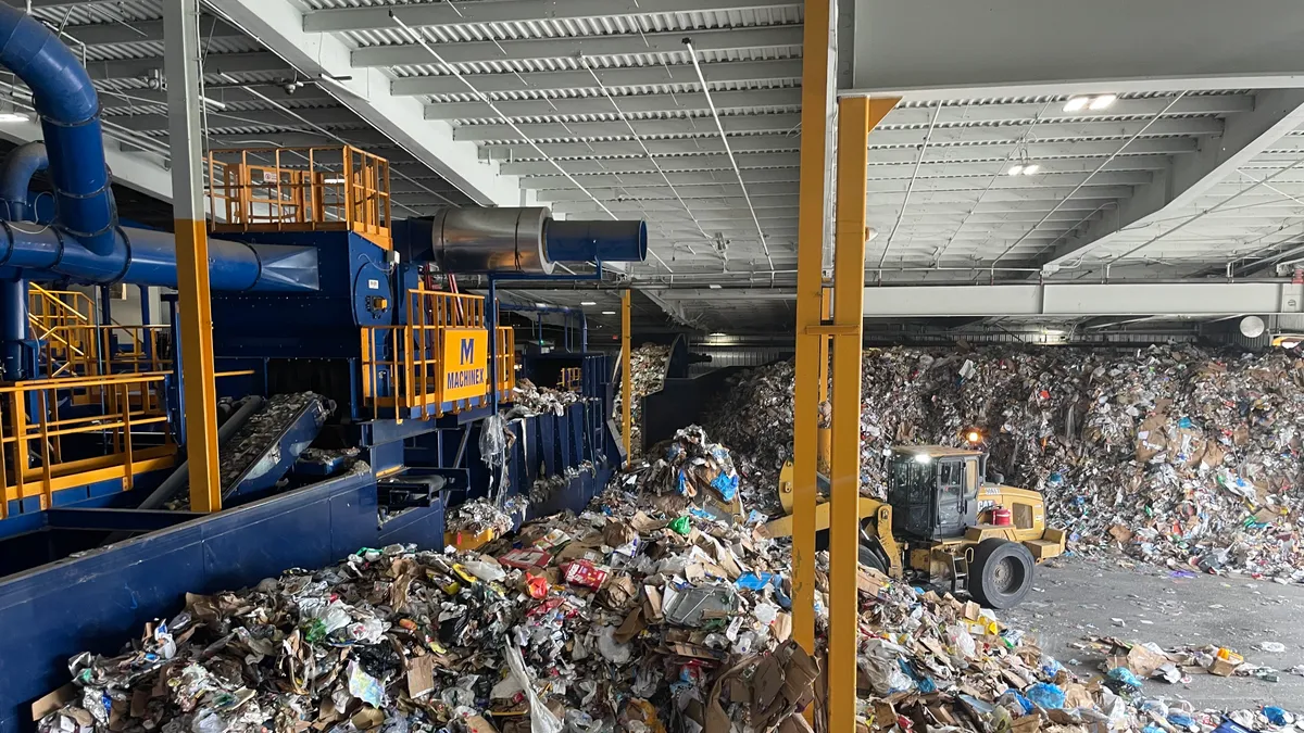 Piles of recyclable material being fed by heavy equipment into a recycling facility