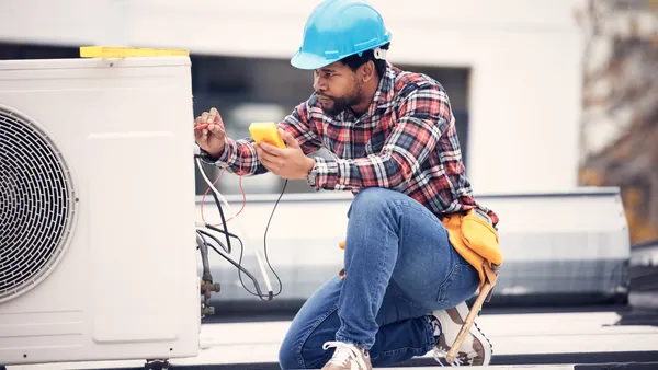 An electrical services contractor is seen working on an electrical power generator to repair an air conditioner.