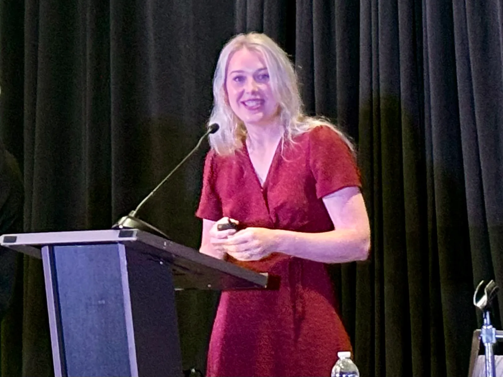 A person is standing behind a podium. A blue curtain is on the wall behind them