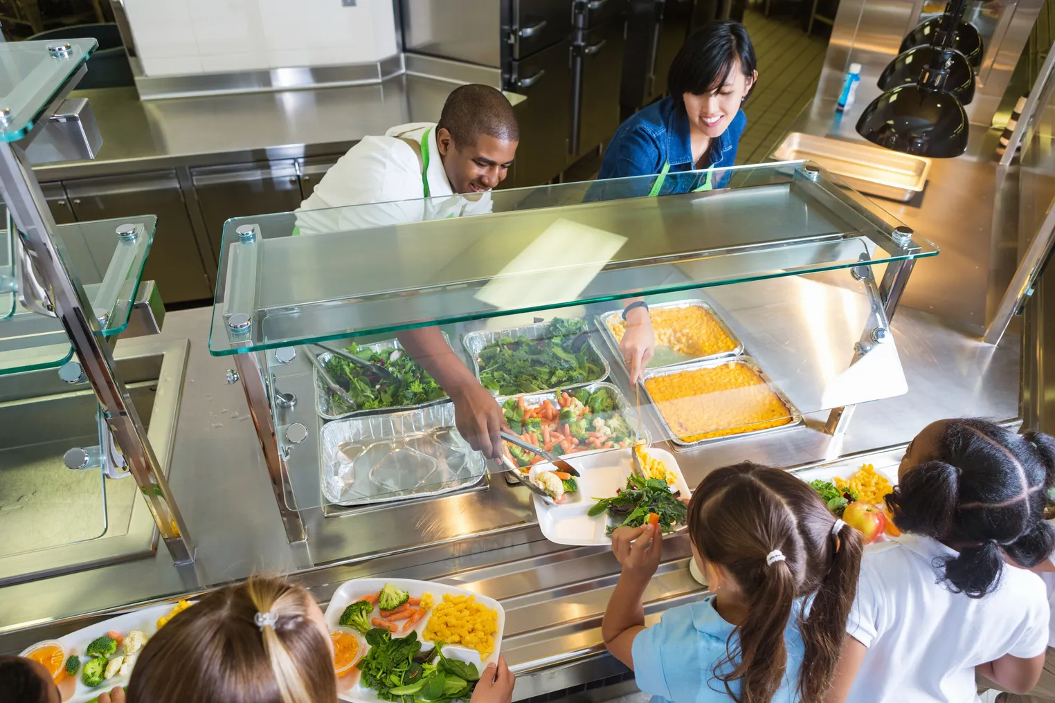 Two school foodservice employees serve food to students in line at a cafeteria.