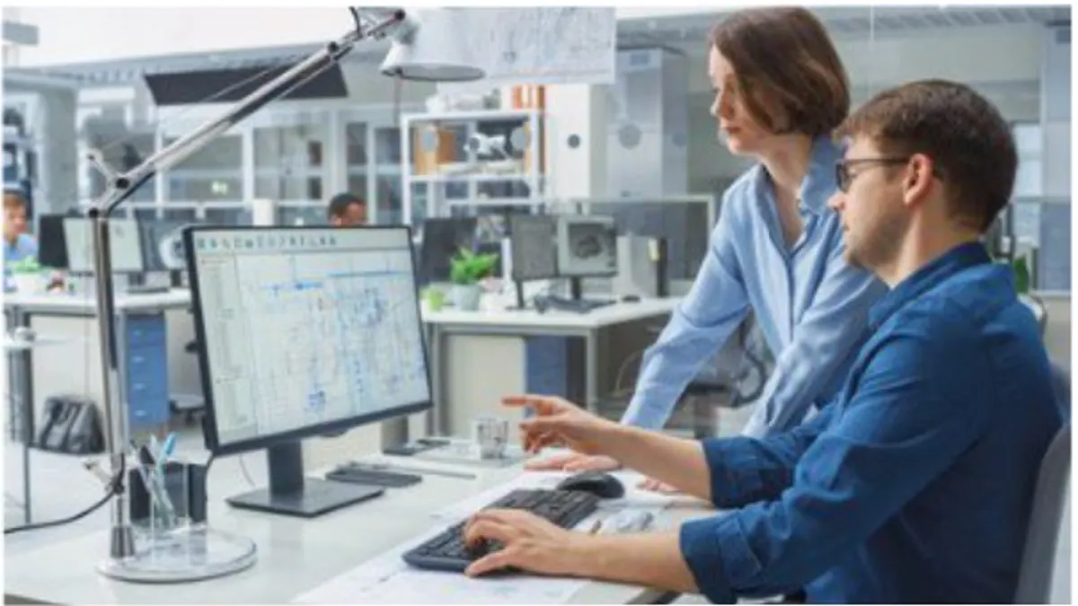 Engineer talking with a project manager while working on a desktop computer